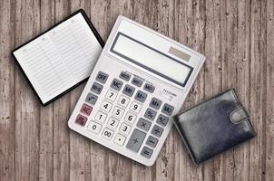 Office flat lay composition with calculator, address book and black purse on brown wooden table background with top view. Accountant paperwork concept photo