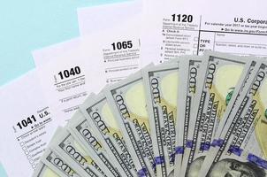 los formularios de impuestos se encuentran cerca de los billetes de cien dólares y la pluma azul sobre un fondo azul claro. declaración de la renta foto