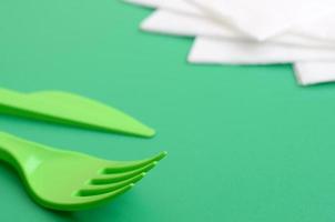 Disposable plastic cutlery green. Plastic fork and knife lie on a green background surface next to napkins photo