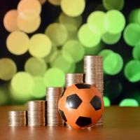 Soccer ball and stacks of golden coins in growth graph on the blurred bokeh background photo