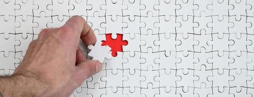 The texture of a white puzzle puzzle in the assembled state with one missing element that the male hand puts in photo