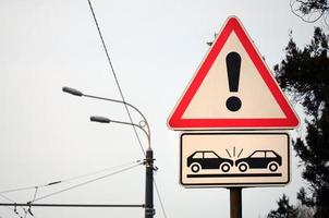 High risk of collision. A road sign with an exclamation point and two cars that crashed into each other photo