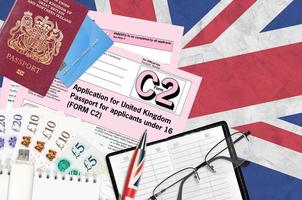 English form C2 Application for United Kingdom passport for applicants under 16 lies on table with office items. UK passport paperwork photo