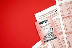 Red lottery ticket with dice lies on pink gambling sheets with numbers for marking to play lottery. Lottery playing concept or gambling addiction. Close up photo