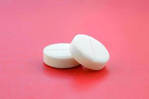 A few white tablets lie on a bright red background surface. Background image on medical and pharmaceutical topics photo