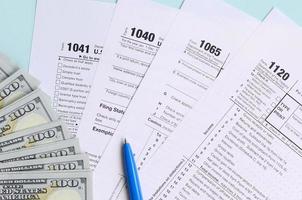 Tax forms lies near hundred dollar bills and blue pen on a light blue background. Income tax return photo