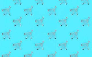 Shopping addiction, shopping lover or shopaholic concept. Many small empty shopping carts perform a pattern on a pastel colored paper background. Flat lay composition, top view photo