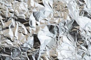 Thin wrinkled sheet of crushed tin aluminum silver foil background with shiny crumpled surface for texture photo