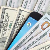 KHARKOV, UKRAINE - JULY 2, 2021 Smartphone screen with Google app and lot of hundred dollar bills. Business and social networking concept photo