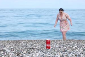 ANTALYA, TURKEY - MAY 18, 2021 Original Coca Cola red tin can lies on small round pebble stones close to sea shore. Coca-cola can and woman on beach photo