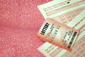 Red lottery ticket lies on pink gambling sheets with numbers for marking to play lottery. Lottery playing concept or gambling addiction. Close up photo