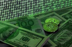 Two bitcoins lies on a pile of dollar bills on the background of a monitor depicting a binary code of bright green zeros and one units on a black background. Low key lighting photo
