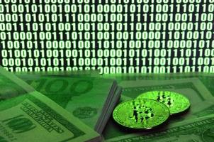 Two bitcoins lies on a pile of dollar bills on the background of a monitor depicting a binary code of bright green zeros and one units on a black background. Low key lighting photo
