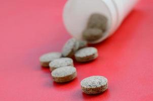 Several brown tablets fall out of the plastic jar on the red surface. Background image on medical and pharmaceutical topics photo