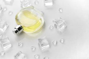 frasco amarillo de perfume femenino, fotografía objetiva del frasco de perfume en cubitos de hielo y agua sobre una mesa blanca. vista desde arriba. foto de producto de maqueta, concepto de frescura