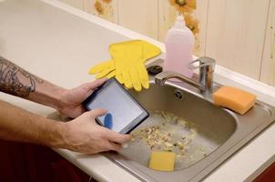 The landlord uses the tablet to call a cleaner in order to clean the clogged kitchen sink photo