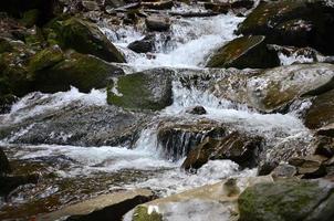 Close-up image of a small wild waterfall in the form of short streams of water between mountain stones photo