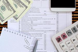 Composition of items lying on the 1040 tax form. Dollar bills, pen, calculator, smartphone, paper clip and notepad. The time to pay taxes photo