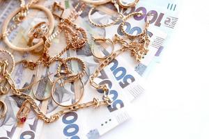 Many expensive golden jewerly rings, earrings and necklaces with big amount of Ukrainian money bills. Pawnshop or jewerly shop concept. Jewelry trading photo