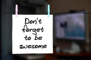 Don't forget to be awesome. Note is written on a white sticker that hangs with a clothespin on a rope on a background of office interior photo