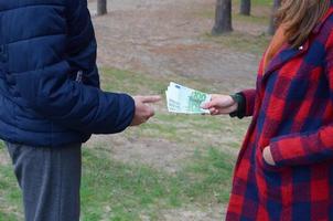 chica transfiere billetes de euro a manos de un joven en el bosque. concepto de robo o transacción de trato ilegal foto