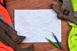 A crumpled sheet of paper with two pencils surrounded by green and orange working uniforms and adjustable wrenches photo