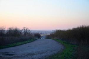 Dawn in the village. Asphalt road, leaving far into the distance among the fields photo