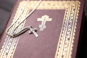 collar de plata con cruz crucifijo en el libro de la santa biblia cristiana sobre una mesa de madera negra. pidiendo bendiciones de dios con el poder de la santidad, que trae suerte foto
