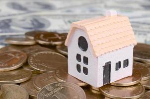 Mini house model on big coins stack on many dollar bills as background photo