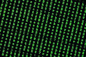 Macro shot of a glitch on the monitor of an office computer. The concept of introducing a virus into a personal data keeper. Stream of random green symbols on a black background photo