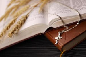 Silver necklace with crucifix cross on christian holy bible book on black wooden table. Asking blessings from God with the power of holiness photo