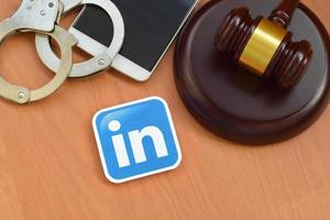KHARKOV, UKRAINE - JULY 2, 2021 Linkedin paper logo lies with wooden judge gavel, smartphone and handcuffs. Entertainment lawsuit concept photo