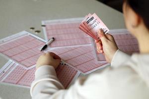 llenando un boleto de lotería. una mujer joven sostiene el billete de lotería con una fila completa de números en el fondo de las hojas en blanco de la lotería. foto