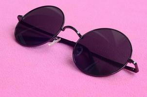 elegantes gafas de sol negras con gafas redondas se encuentran sobre una manta hecha de suave y esponjosa tela de lana rosa claro. imagen de fondo de moda en colores femeninos foto