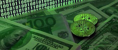 Two bitcoins lies on a pile of dollar bills on the background of a monitor depicting a binary code of bright green zeros and one units on a black background. Low key lighting photo