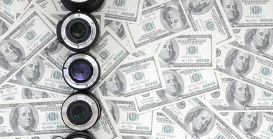 A few photographic lenses lies on the background of a lot of dollar bills. Space for text photo