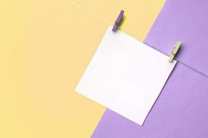 A piece of paper is hanging on a rope with pegs on texture background of fashion pastel yellow and violet colors photo
