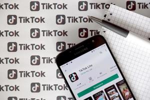 TERNOPIL, UKRAINE - MAY 2, 2022 Tik Tok smartphone app on screen and Many TikTok logo printed on paper. Tiktok or Douyin is a famous Chinese short-form video hosting service owned by ByteDance photo