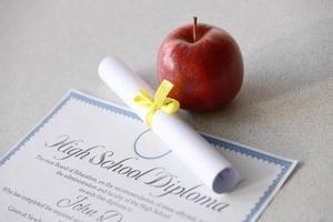 A high school diploma lies on table with small scroll and red apple. Education documents photo