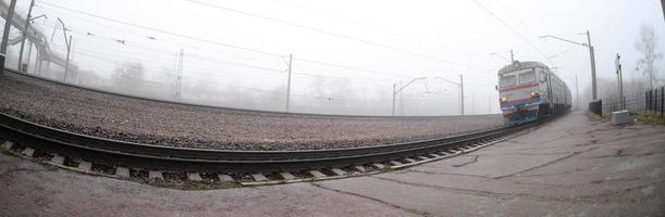 The Ukrainian suburban train rushes along the railway in a misty morning. Fisheye photo with increased distortion