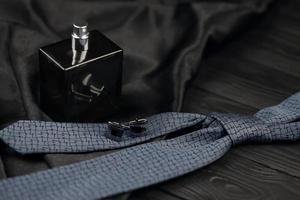 una botella de colonia masculina y gemelos con corbata azul se encuentran sobre un fondo de tela negra de lujo sobre una mesa de madera. accesorios para hombre foto