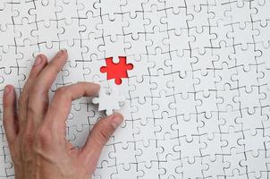 The texture of a white puzzle puzzle in the assembled state with one missing element that the male hand puts in photo