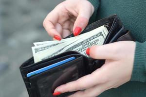 Woman hands with red nails holds black mens purse with many US hundred dollars bills. Concept of salary earnings or counting money photo