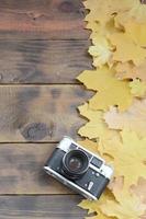 The old camera among a set of yellowing fallen autumn leaves on a background surface of natural wooden boards of dark brown color photo