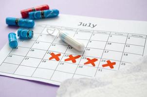 Menstrual pads and tampons on menstruation period calendar with red cross marks lies on lilac background photo