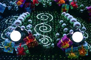 A fragment of a huge Christmas tree with many ornaments, gift boxes and luminous lamps. Photo of a decorated Christmas tree close-up