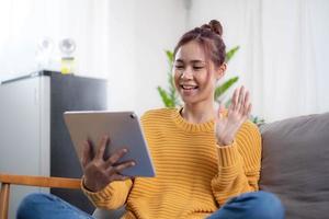 Relaxed young mixed race woman in sofa smiling content, happy and reading on tablet pc at home in couch. Lifestyle image of beautiful mixed Asian girl relaxing smiling happy photo