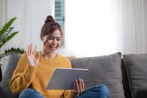 Relaxed young mixed race woman in sofa smiling content, happy and reading on tablet pc at home in couch. Lifestyle image of beautiful mixed Asian girl relaxing smiling happy photo