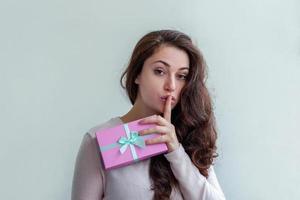 Young positive woman holding small pink gift box isolated on white background. Preparation for holiday. Girl looking happy and excited. Christmas birthday valentine celebration present concept. photo