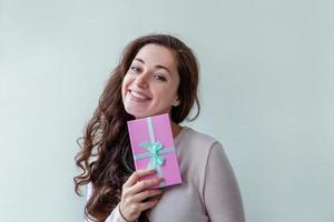 joven positiva sosteniendo una pequeña caja de regalo rosa aislada de fondo blanco. preparación para las vacaciones. chica que parece feliz y emocionada. navidad cumpleaños san valentín celebración presente concepto. foto